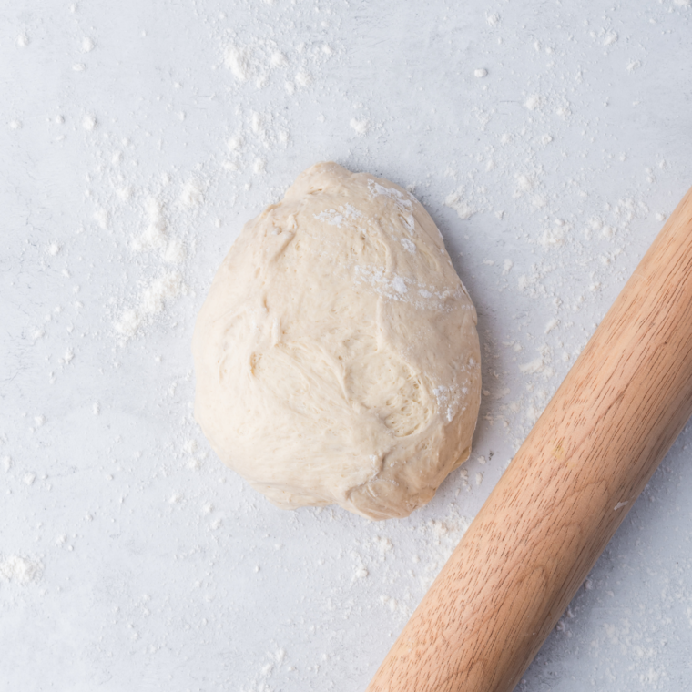 Pizza dough on a floured counter being cut into 12 equal pieces with a bench scraper for air fryer garlic knots.