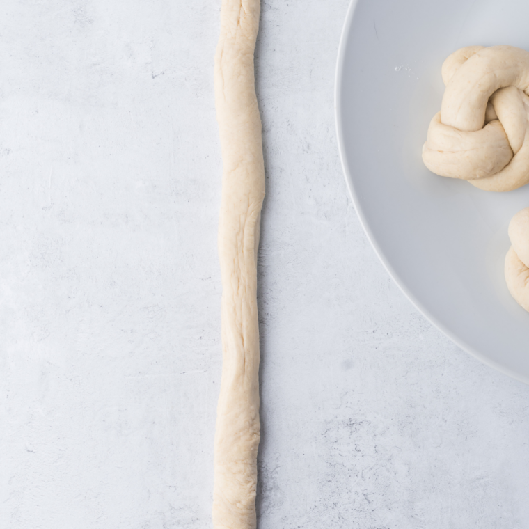 Hands rolling small dough portions into smooth 6-inch ropes on a lightly floured surface for garlic knots.