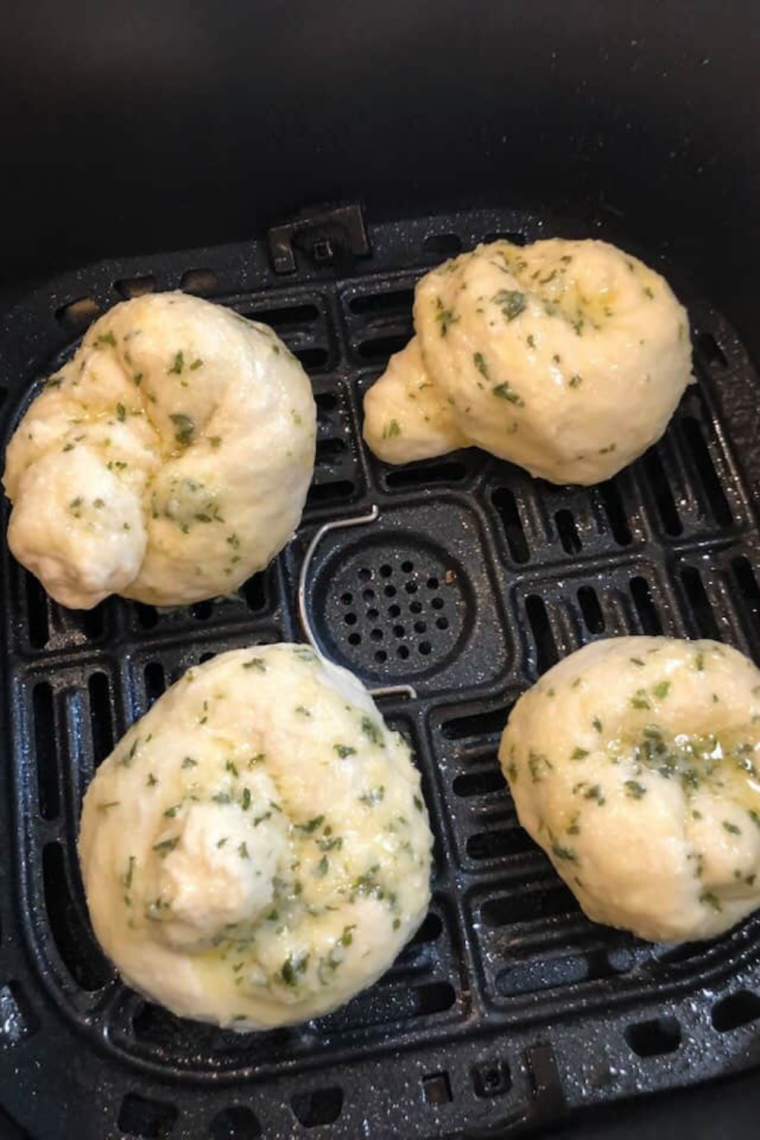 Unbaked garlic knots arranged in a single layer inside an air fryer basket, cooking until golden brown.