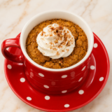 Air fryer pumpkin mug cake in a white ceramic mug topped with whipped cream and a dusting of pumpkin spice