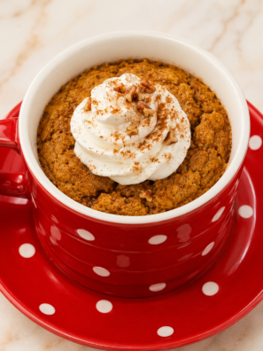 Air fryer pumpkin mug cake in a white ceramic mug topped with whipped cream and a dusting of pumpkin spice