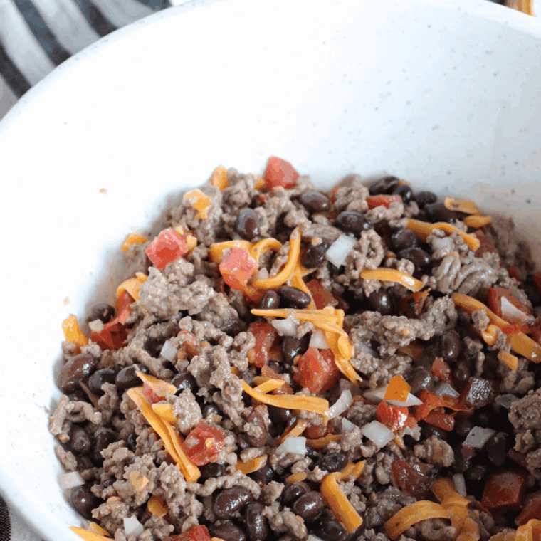 Ground beef mixed with Rotel, black beans, onions, and shredded cheese in a bowl.