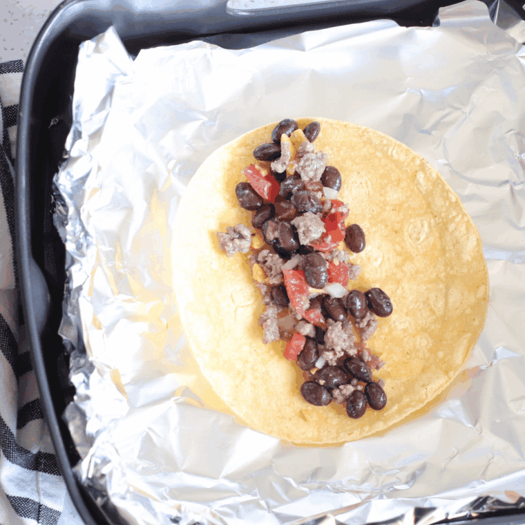 Corn tortillas filled with beef mixture and rolled in foil-lined air fryer basket.
