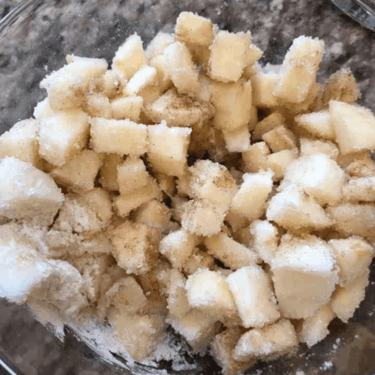 Mixing peeled, diced apples with sugar, flour, and cinnamon in a large bowl, preparing air fryer muffin tin with cooking spray.