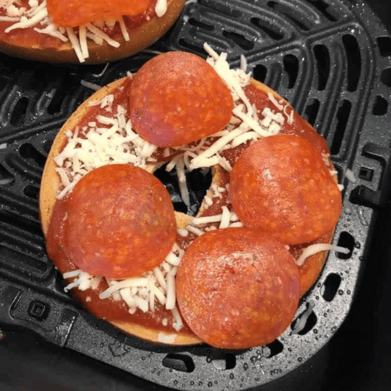 overhead process shot: pizza bagels in air fryer basket with cheese and pepperoni