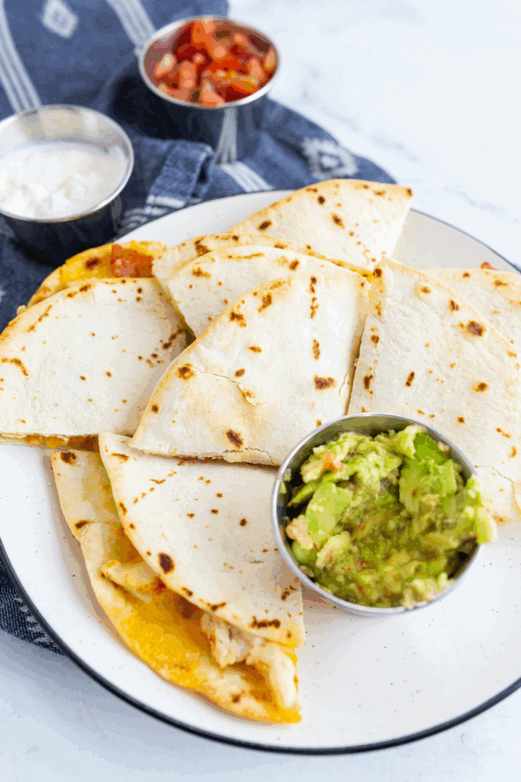 Golden brown air fryer chicken quesadilla slices stacked on a plate with melted cheese and chicken inside.