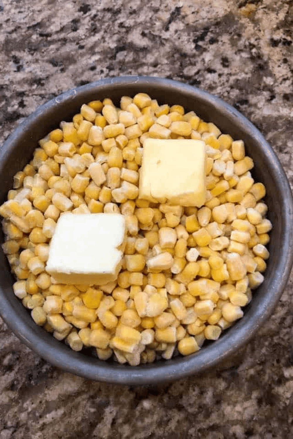 Frozen corn in an air fryer pan sprayed with olive oil, topped with butter and sprinkled with sugar, ready to cook.