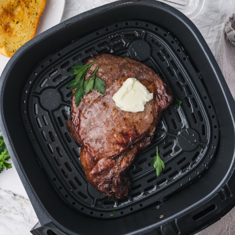 Air fryer basket with a frozen steak seasoned and ready to cook, demonstrating the air frying process.