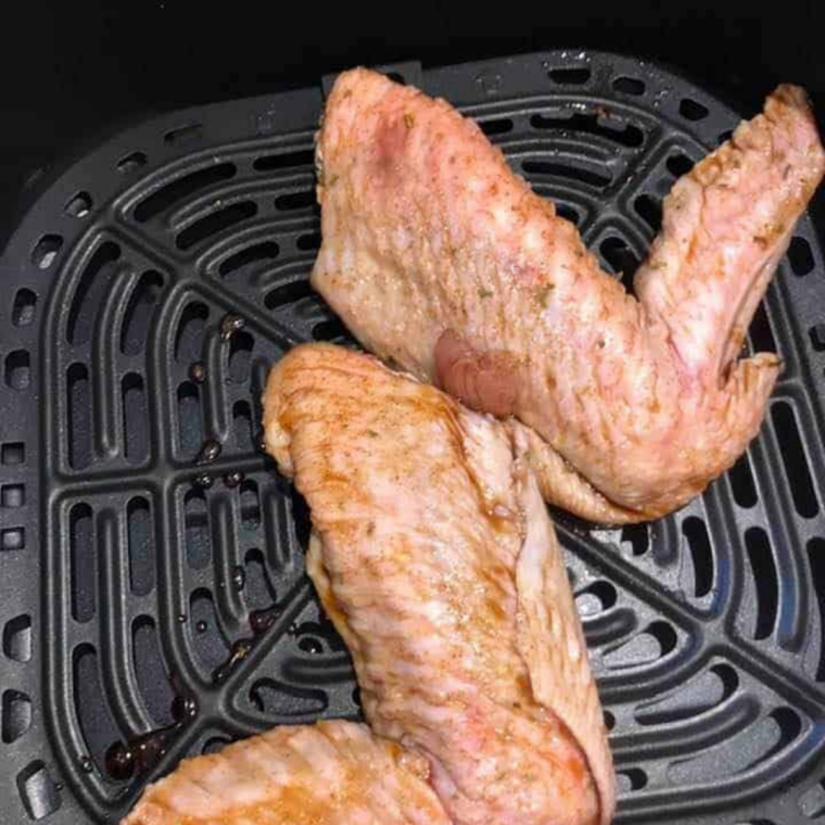 air fryer turkey wings cooking and being brushed with honey garlic glaze mid-cook
