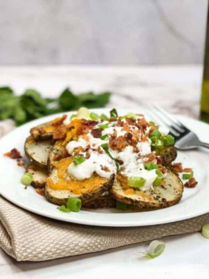 Plate of Air Fryer Loaded Baked Potato Foil Packs featuring crispy, golden potatoes topped with melted cheese, crispy bacon bits, and fresh chives.