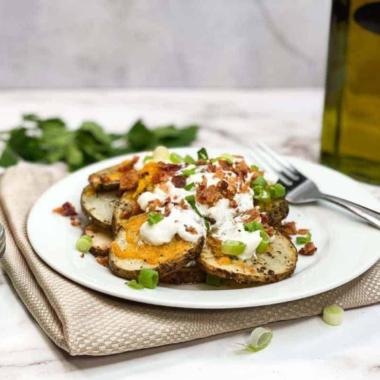 Plate of Air Fryer Loaded Baked Potato Foil Packs featuring crispy, golden potatoes topped with melted cheese, crispy bacon bits, and fresh chives.