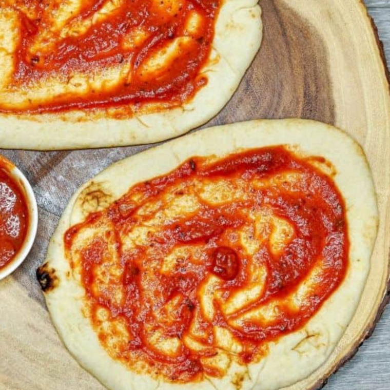 Adding shredded mozzarella and buffalo-coated diced chicken on top of naan bread.