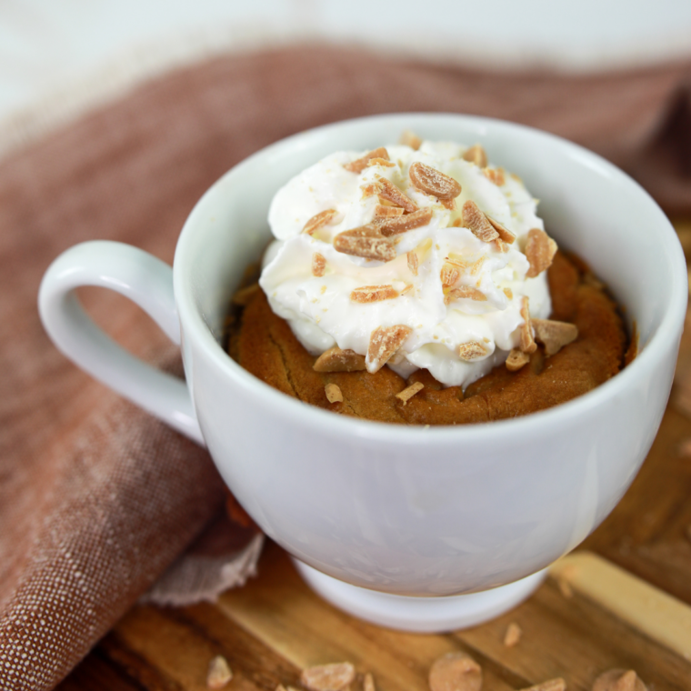 Single serving air fryer peanut butter mug cake in a ceramic mug beside a jar of peanut butter 