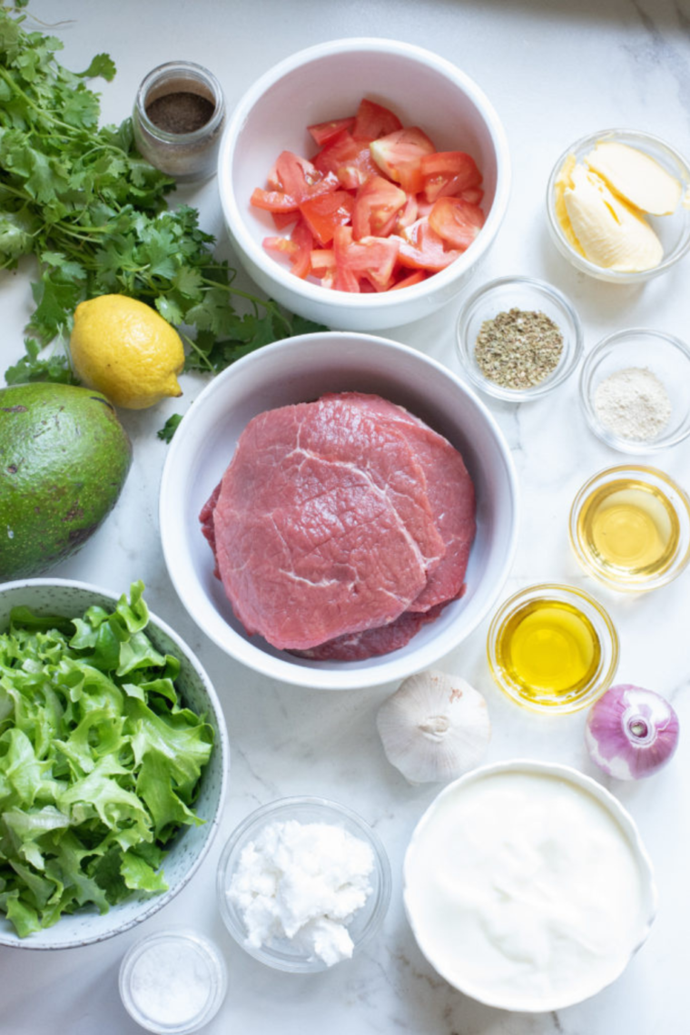 Ingredients for Air Fryer Steak Salad arranged on a kitchen table, including fresh vegetables, steak, and seasonings.