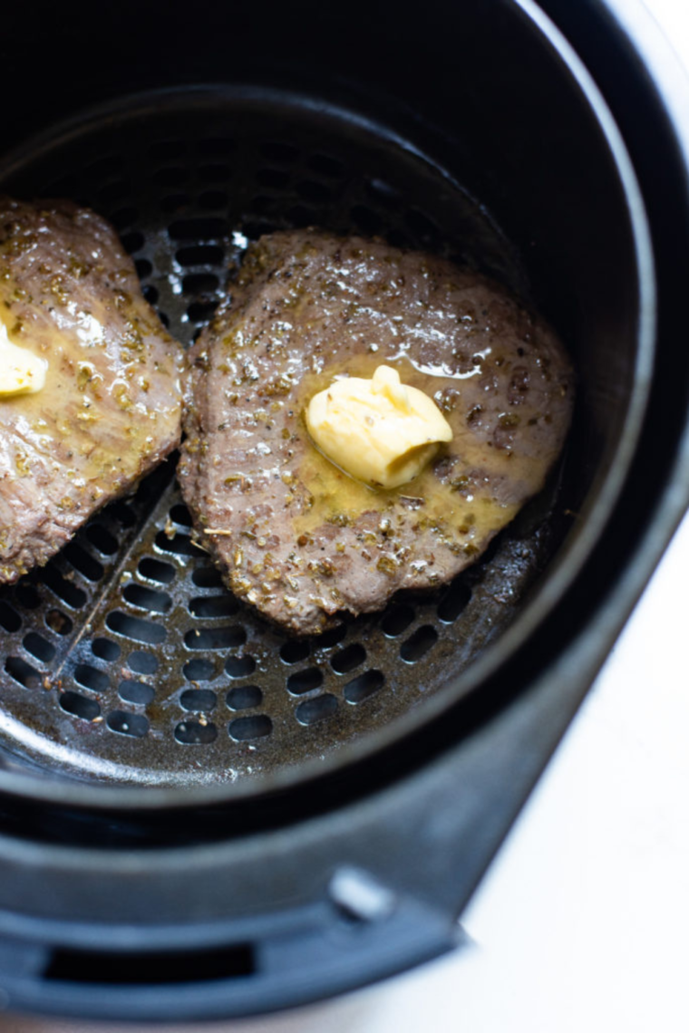 Marinating the steak with salt, pepper, garlic, basil, and oil, then cooking in the air fryer for a perfectly seared result.