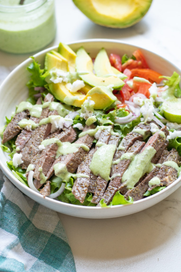 Air fryer steak salad with marinated steak, fresh romaine lettuce, avocado, tomatoes, and cilantro dressing, served on a plate.