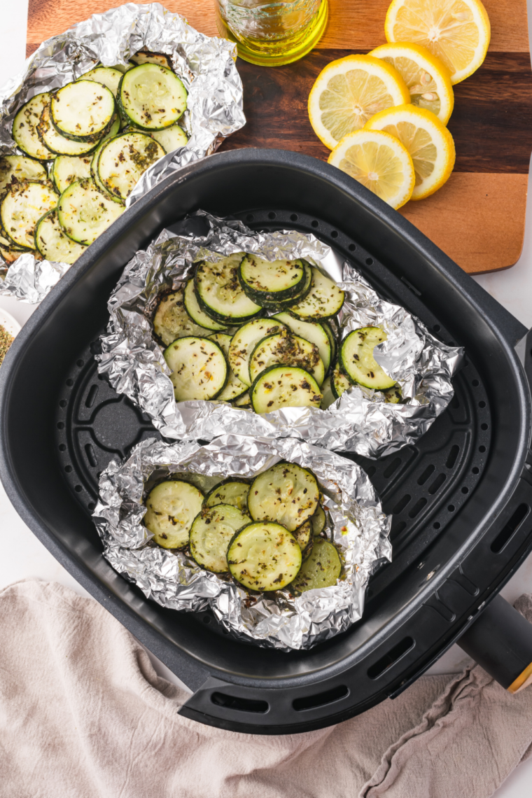 Opening a zucchini foil packet to reveal tender, seasoned vegetables.