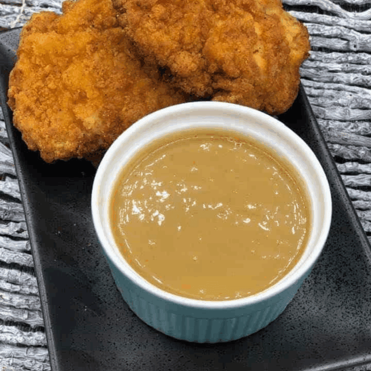 Homemade Carolina honey mustard BBQ sauce in a glass jar with a brush and fresh ingredients nearby.