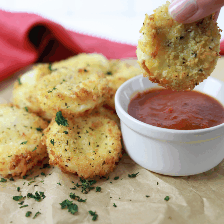 Crispy golden Air Fryer Babybel cheese being pulled apart to show the melted, gooey interior, next to a bowl of marinara sauce.