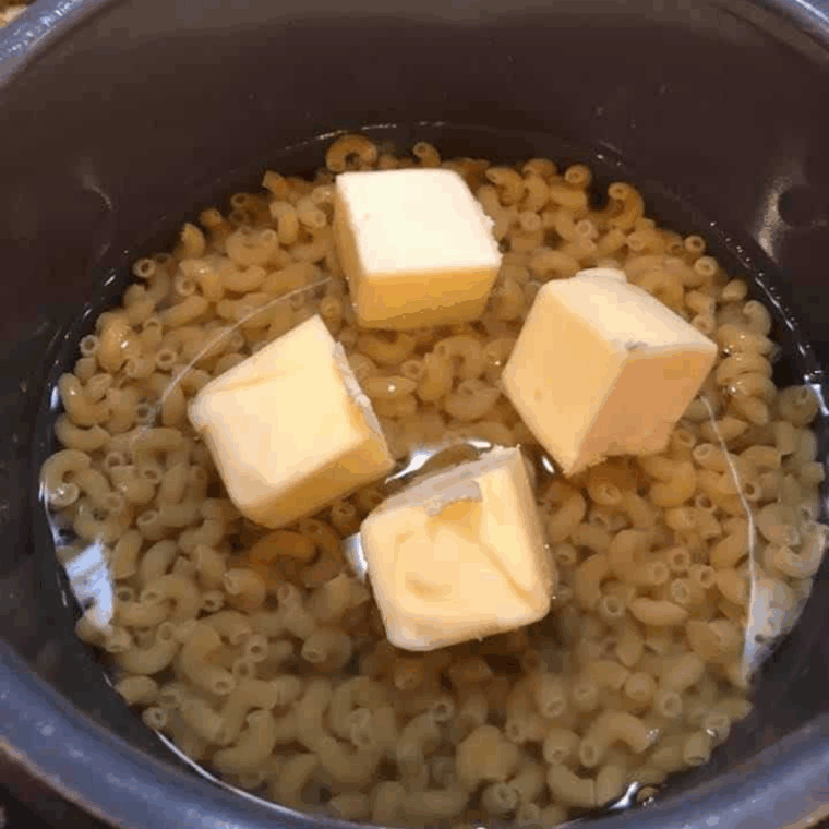 Elbow macaroni in Instant Pot with water and butter squares on top ready for cooking