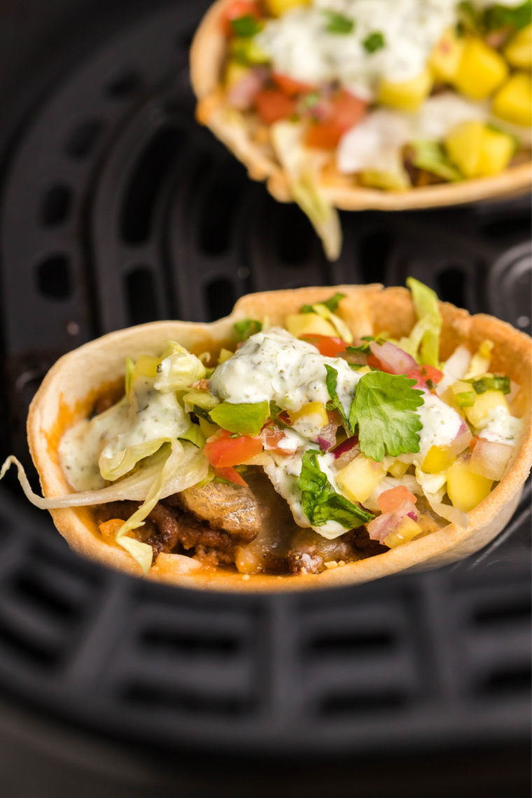 Air fryer taco cups cooking in the basket until the cheese melts and edges crisp