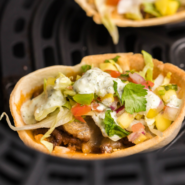 Close-up of finished air fryer taco cups with toppings and cilantro lime sour cream drizzle.