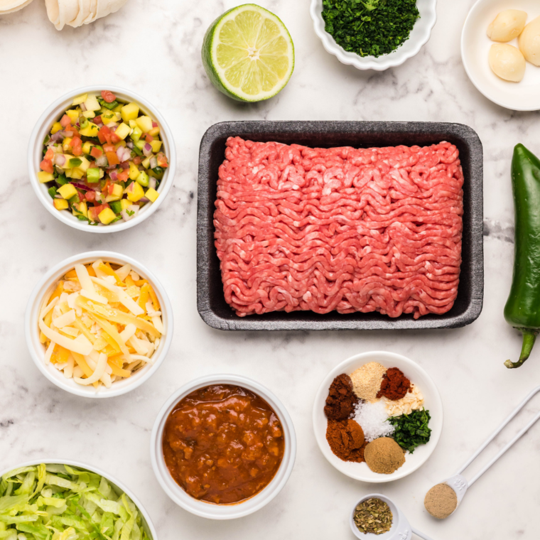 Ingredients for air fryer taco cups including ground beef, mini taco bowls, cheese, and cilantro lime sour cream.