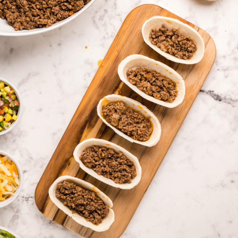 Air fryer taco cups cooking in the basket until the cheese melts and edges crisp