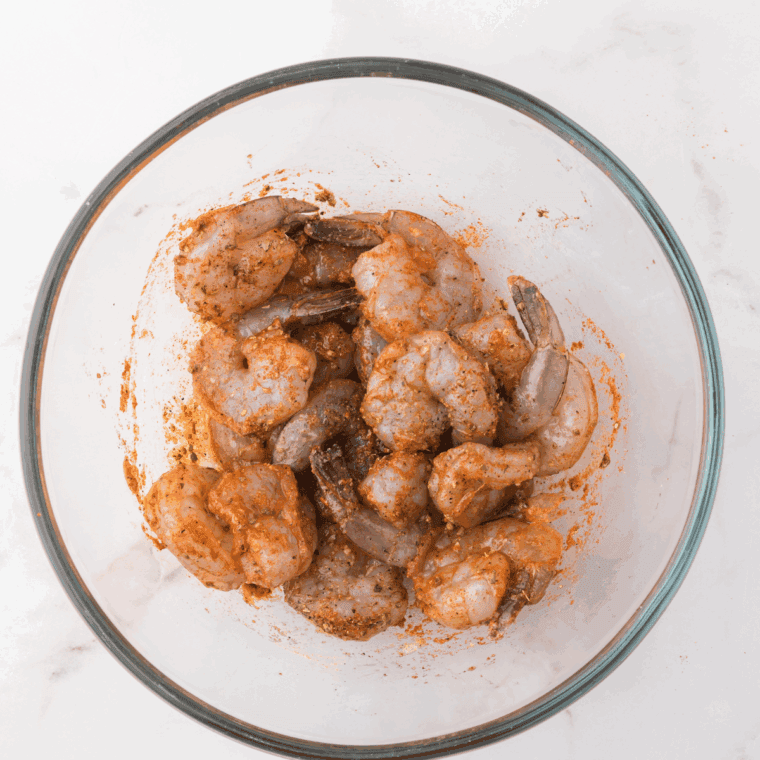 Shrimp tossed in olive oil and spices in a mixing bowl.