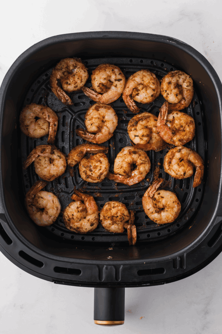 Shrimp cooking in air fryer, shaking basket halfway through.