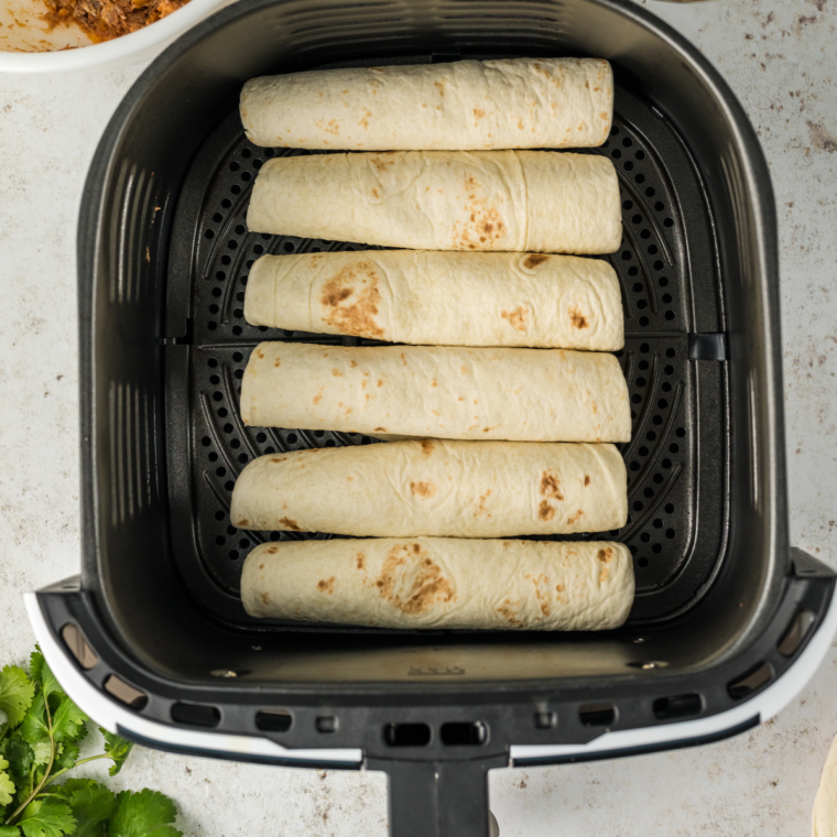 Air fryer basket filled with flautas cooking until golden brown and crispy.