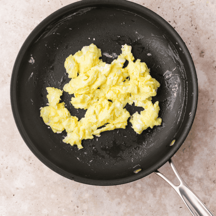 Cracking eggs into a bowl, whisking them with a fork, and cooking scrambled eggs with melted butter in a skillet.