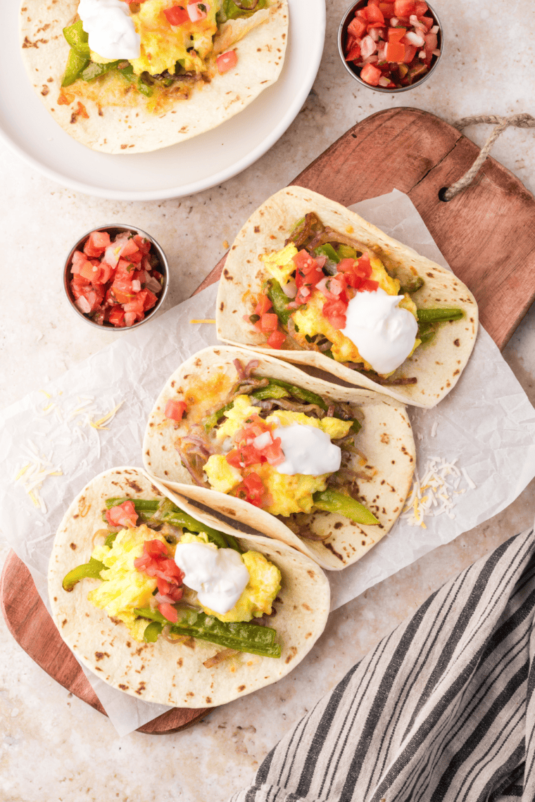 Air Fryer Breakfast Tacos with scrambled eggs, sautéed vegetables, and shredded cheese on a tortilla, ready to be served with toppings like sour cream and tomatoes.