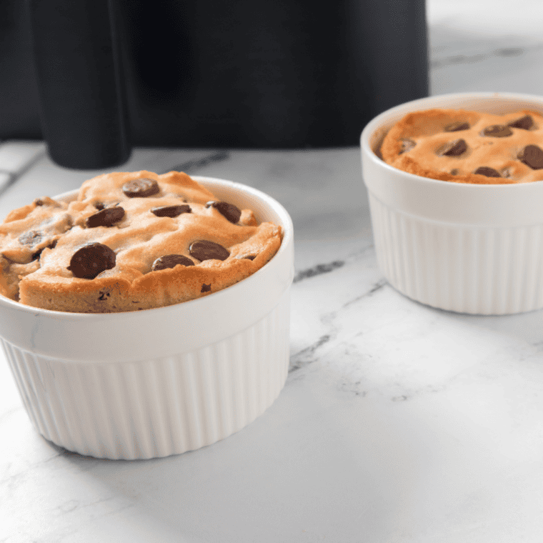 Warm chocolate chip cookie in a cup made in the air fryer, gooey center with melted chocolate chips on top, served in a small dish.