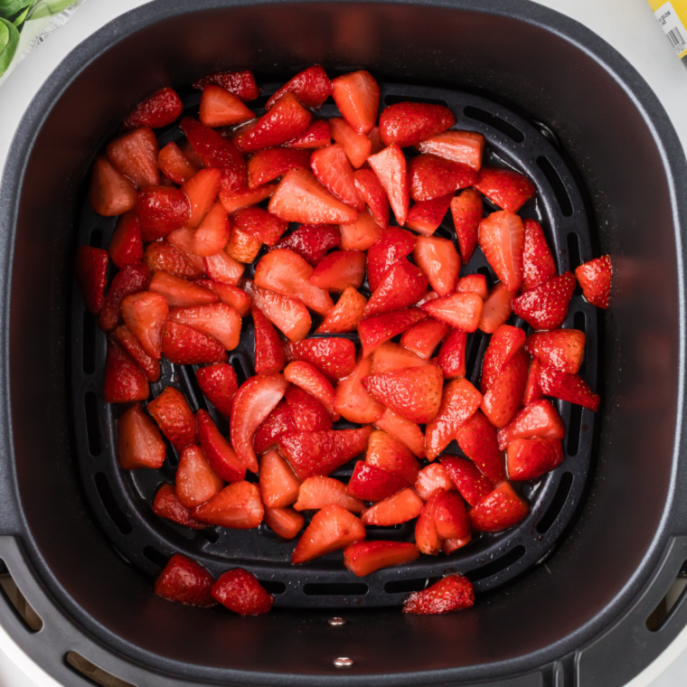 Halved strawberries tossed with sugar and lemon juice in an air fryer basket