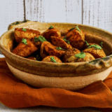 Crispy air fryer curry potatoes with golden edges in a white bowl, topped with fresh cilantro