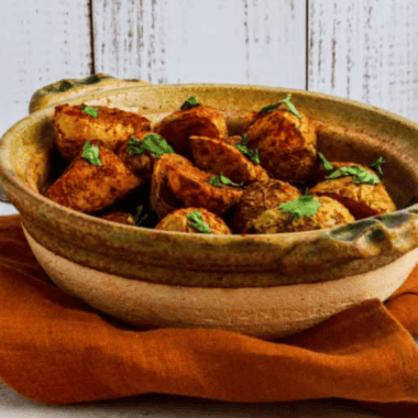 Crispy air fryer curry potatoes with golden edges in a white bowl, topped with fresh cilantro