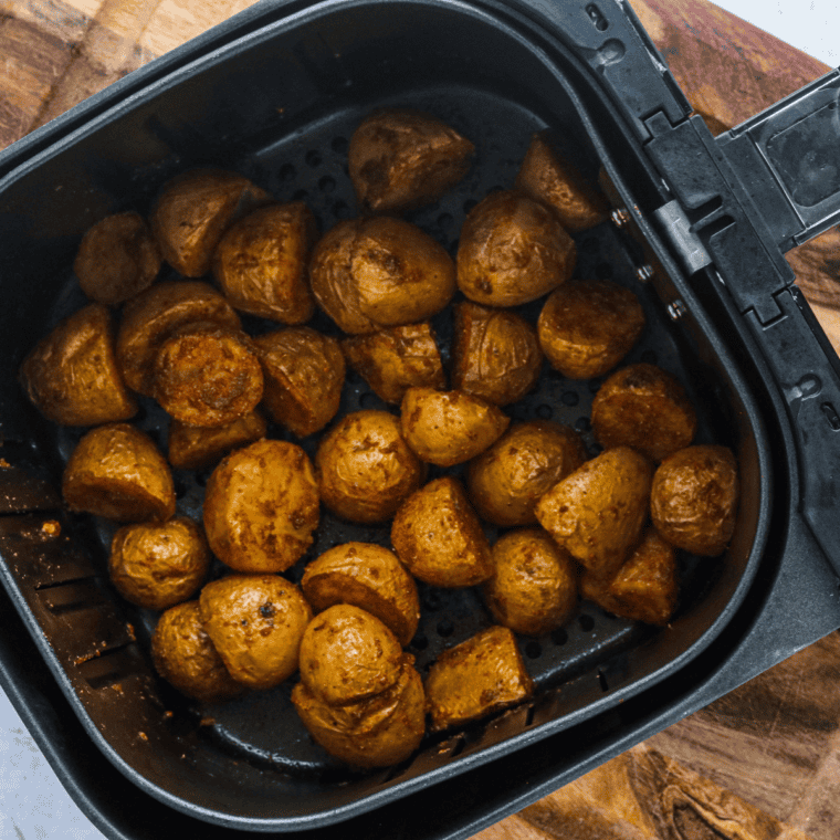 Curry potatoes with deep golden browned edges in the air fryer basket after cooking