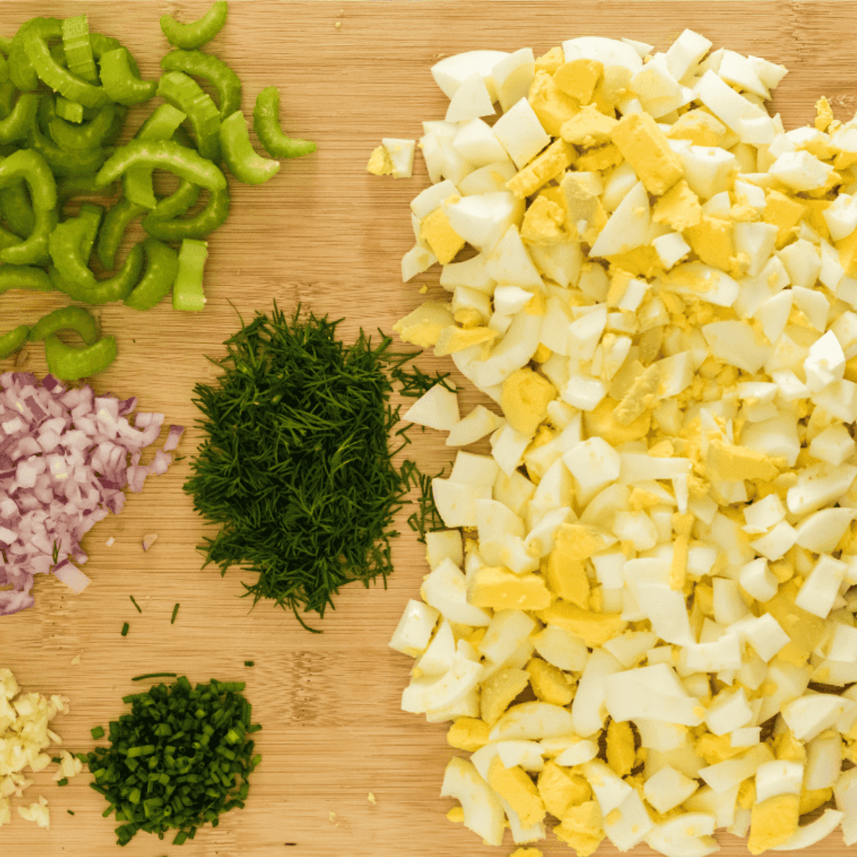 Chopped hard-boiled eggs in a bowl with freshly chopped celery, dill, and chives, ready to mix for egg salad.