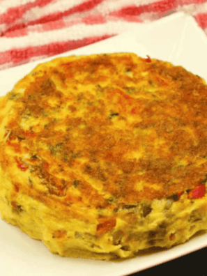 Golden air fryer frittata with bell peppers, onions, and melted cheddar in a 7-inch cake pan, one wedge sliced out