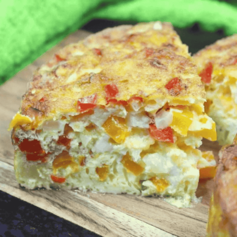 Slice of air fryer frittata on a white plate with golden top, melted cheddar, bell peppers, and onions visible