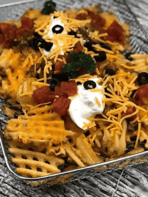 Air fryer loaded waffle fries topped with melted cheddar, bacon, jalapeños, and sour cream on a white platter