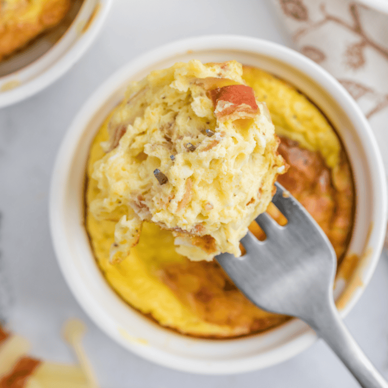 Fork lifting a bite of fluffy air fryer cheesy egg mug omelet with melted cheddar stretching from the ramekin