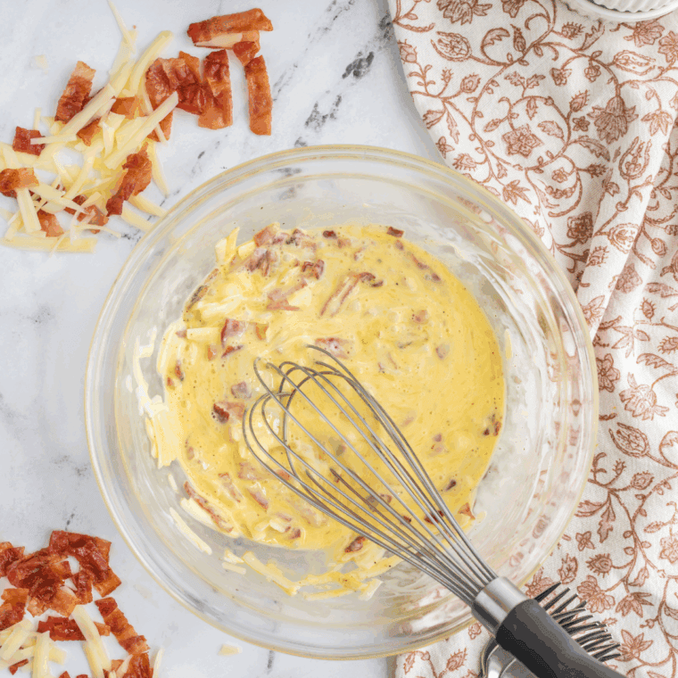 Whisking together eggs, diced bell peppers, mushrooms, shredded cheese, heavy cream, salt, and pepper in a mixing bowl.