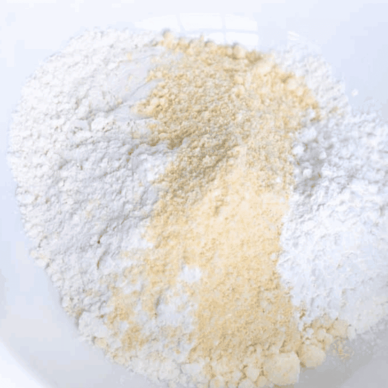 Large bowl filled with flour, corn muffin mix, cornstarch, seasonings, and egg being mixed into batter.