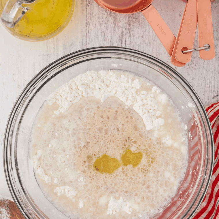 A stainless steel sifter over a glass bowl containing flour, ginger, cinnamon, and baking soda to ensure a smooth muffin batter.