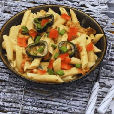 Creamy Instant Pot Cajun Chicken Alfredo served with penne pasta, sliced chicken, parmesan cheese, and Cajun seasoning in a white bowl.