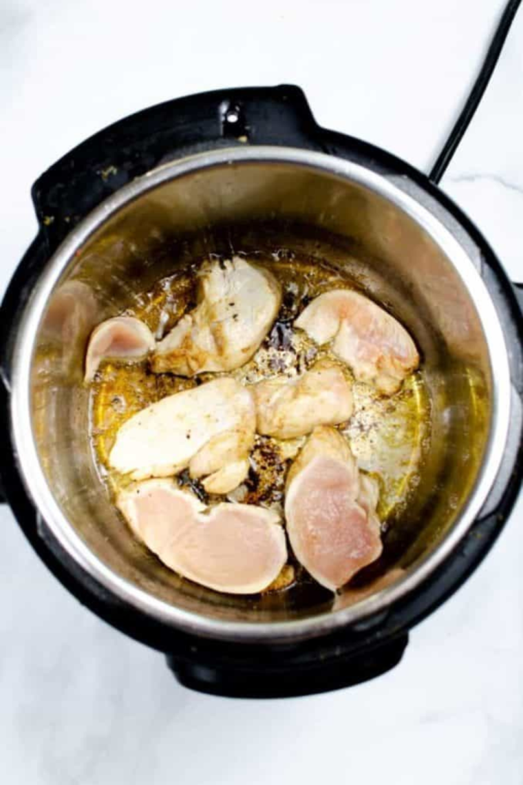 "Seasoned chicken strips cooking in an Instant Pot on sauté mode with olive oil, checked for doneness with a meat thermometer."