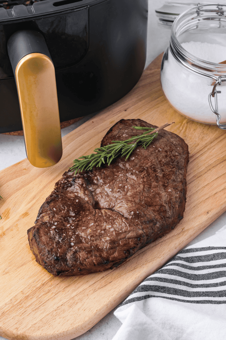 Perfectly cooked air fryer sirloin steak, golden-brown crust, juicy interior, served on a cutting board with herbs and garlic.
