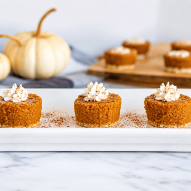 Pumpkin pie bites topped with whipped cream arranged on a slate serving board